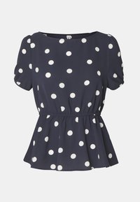 Blouse bleu marine avec des pois blancs, manches courtes bouffantes, encolure ronde et taille froncée pour un effet peplum. Texture de tissu douce.