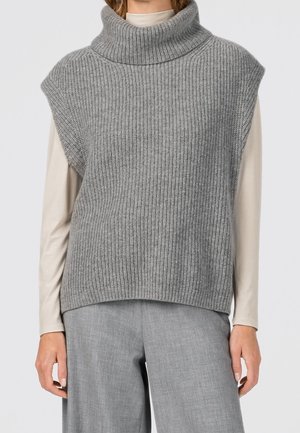 Hihaton paksu harmaa neuleliivi poolokauluksella, yllä beige pitkähihoinen paita ja harmaat leveälahkeiset housut.