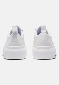 Les baskets blanches présentent un design épuré avec une semelle épaisse et texturée ainsi qu'une languette à l'arrière. Matière supérieure lisse avec des accents subtils.