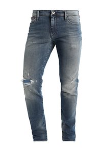 Vaqueros de mezclilla en un azul deslavado con detalles desgastados y una rodilla rasgada. Diseño estándar de cinco bolsillos con cierre de botón y trabillas para el cinturón.