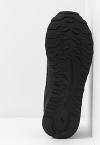 Svart sportskor med en texturerad gummisula med ett zickzackmönster och en övre del i mesh, prydd med grå detaljer och logotyp.