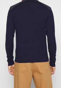 Námořnicky modrý pletený svetr s dlouhými rukávy, žebrovaným lemem a akcenty na ramenou z texturovaného materiálu. Klasický střih s minimálním zdobením.