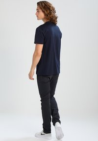 Camiseta de manga corta azul marino combinada con pantalones negros, mostrando un ajuste relajado y una textura suave. Modelo visto desde atrás, llevando zapatillas blancas.