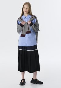 Lichtblauw gestreepte blouse met knoopsluiting, gelaagde grijze cardigan, zwarte rok met plooien en kantafwerking, gecombineerd met zwarte sneakers.