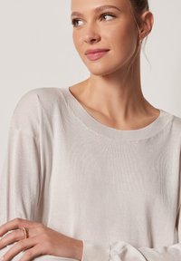 Jasnobeżowy sweter z długim rękawem o szerokim okrągłym dekolcie, wykonany z miękkiego, teksturowanego materiału. Posiada luźne rękawy i gładkie wykończenie.