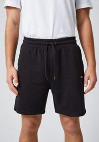 Zwarte katoenen shorts met een elastische tailleband en trekkoord, voorzien van een zijlogo en een gladde textuur. Casual ontwerp met een knie-lengte snit.