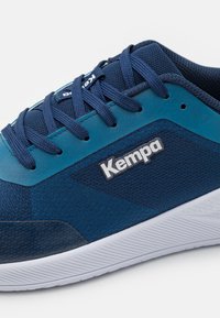 Marineblå og teal sportssko med mesh-overdel og teksturerede mønstre. Har en hvid sål og 'Kempa' logo i sølv på siden.