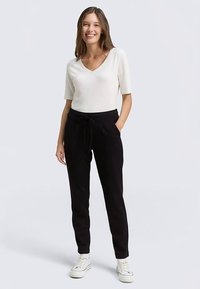 Zwarte joggingbroek met trekkoord in de taille, twee steekzakken aan de zijkant, gecombineerd met een aangesloten wit V-hals T-shirt met korte mouwen. Glad van textuur, casual stijl.