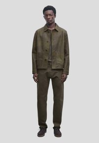 Veste et pantalon vert olive en tissu texturé, avec une veste à col dotée d'un bouton de fermeture et de poches avant.