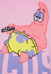 Patrick Star allongé avec une télécommande TV, portant un short jaune-vert à fleurs violettes sur un fond en tissu tricoté rose.