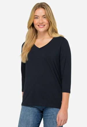 T-shirt blu navy a V con maniche a tre quarti; tessuto morbido e leggero; texture liscia; abbinato a jeans a righe blu chiaro.