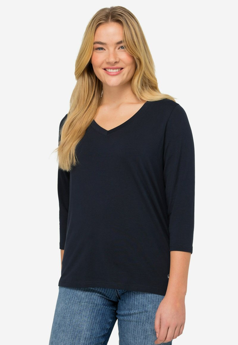 Marineblaues V-Ausschnitt-T-Shirt mit Dreiviertelärmeln; weicher, leichter Stoff; glatte Textur; kombiniert mit hellblauen gestreiften Jeans.