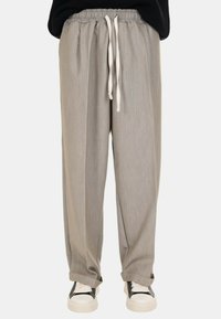 Pantaloni grigio chiaro, larghi e comodi, con cintura elastica e lacci. Realizzati in un tessuto morbido con una consistenza liscia. Indossati con sneakers bianche.