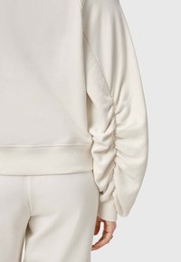 Sudadera de color crema con mangas abullonadas con detalles fruncidos, puños acanalados y un tejido suave y texturizado.