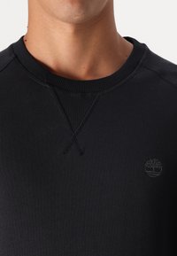 Felpa nera in cotone con collo a costine, caratterizzata da un logo tono su tono. Il tessuto ha una texture liscia ed è leggero.