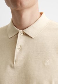 Bežna polo majica iz bombažnega materiala, s klasičnim ovratnikom, dvema gumboma in diskretno izvezenim logotipom na prsih.