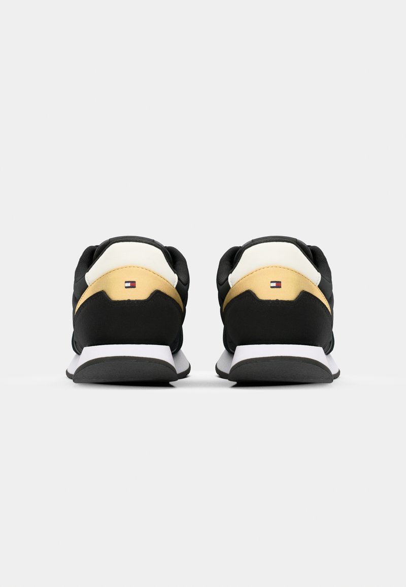 Czarne sneakersy z wyściełanym czarnym obcasem, żółtymi i białymi akcentami oraz białą podeszwą środkową. Gładka tekstura z detalem logo z tyłu.