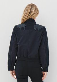 Fekete bombázódzseki bordázott szegéllyel és mandzsettákkal, vállon és ujjakon texturált mintával. Sima anyagból, testhezálló szabással.