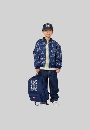 Navy bomber jacket with white floral designs, light green layered shirt, dark jeans, and navy backpack featuring white text and Eiffel Tower graphic.