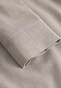 Material gri deschis cu textură netedă, având o manșetă rulată și o cusătură dreaptă. Materialul pare ușor și aerisit.