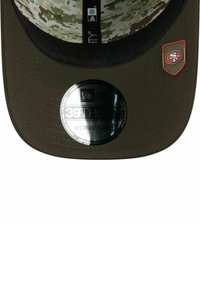 Olivgrüner Hut mit einem camo-musterierten Innenfutter, gebogenem Schirm und einem runden silbernen Aufkleber, der Größe und Marke angibt. Mit Logopatch an der Seite.