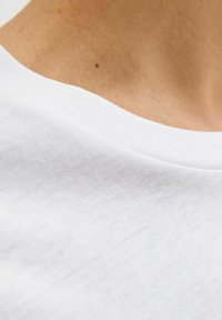 Hvid bomulds t-shirt med rund halsudskæring, der har en glat tekstur og subtile syninger omkring kraven.