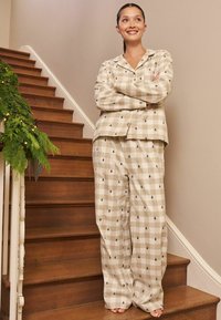 Rutig pyjamas-set i beige med gröna trä-mönster, bestående av en knäppskjorta och löst sittande byxor. Slät tyg på trätrappor.