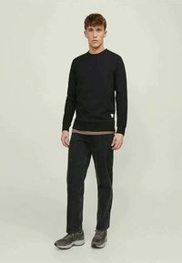 Black long-sleeve sweatshirt made of cotton, paired with dark jeans and gray athletic shoes. Features a ribbed neckline and subtle tag detail.