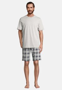 T-shirt en coton gris à manches courtes, associé à un short à carreaux bleu, gris et blanc. Debout pieds nus, les mains sur les côtés.
