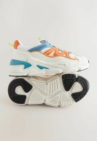 Masywne sneakersy z białej siateczki i syntetycznego materiału, z pomarańczowymi, niebieskimi i zielonymi akcentami, teksturowanymi podeszwami i warstwową konstrukcją.