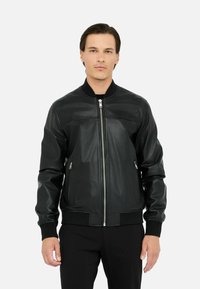 Zwarte leren bomberjack met een ritssluiting aan de voorkant, geribbelde manchetten en twee zijzakken. Glad textuur met minimale stikseldetails.