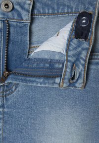 Vaqueros de denim azul claro con cremallera, cierre de botón y costuras en contraste en color arena. Forro interior visible cerca de la cremallera.