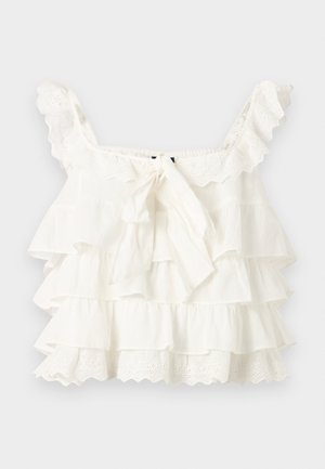 Hvid ærmeløs cropped top med flæser, øjelnedkant og en bindebøjle foran, vist på en lysegrå baggrund.