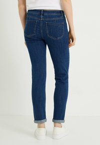 Vaqueros de mezclilla azul con un ajuste entallado, con puños doblados, dos bolsillos traseros y textura de lavado oscuro. Zapatillas blancas completan el conjunto.