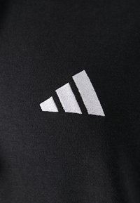 Crna tkanina glatke teksture s istaknutim bijelim izvezenim logotipom, koji se sastoji od tri dijagonalne pruge različitih širina.