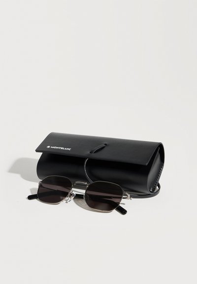 Μαύρα γυαλιά ηλίου Montblanc με ασημένιο πλαίσιο τοποθετημένα μπροστά από μια αντίστοιχη μαύρη δερμάτινη θήκη με το λογότυπο Montblanc σε μια λευκή επιφάνεια.