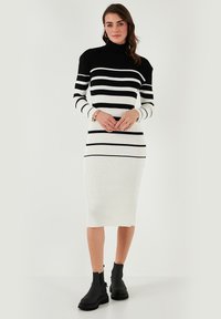 Mustapohjainen raidallinen ribbiknitti turtleneck-mekko, midi-pituinen ja pitkähihaisilla hihoilla, yhdistetty mustiin nilkkasaappaisiin. Suora pinta.