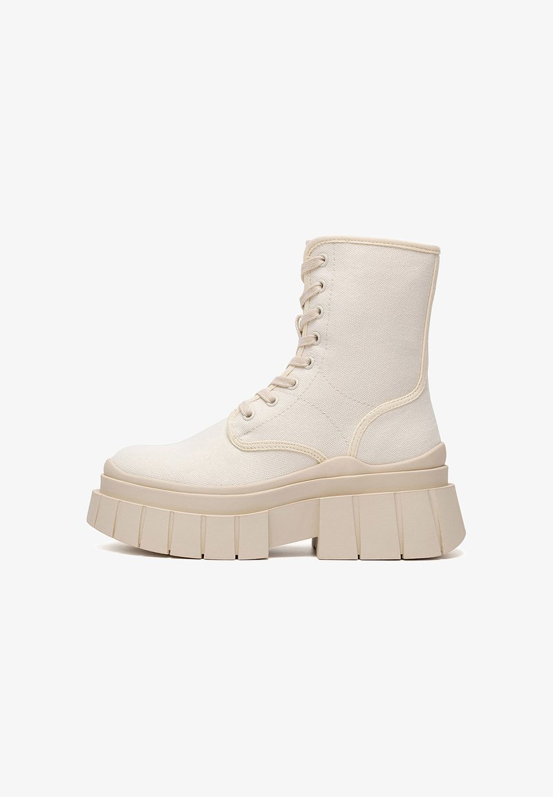 Botines de lona beige con un diseño de perfil alto, suela gruesa con plataforma y detalles texturizados. Presentan punta redonda y cordones.