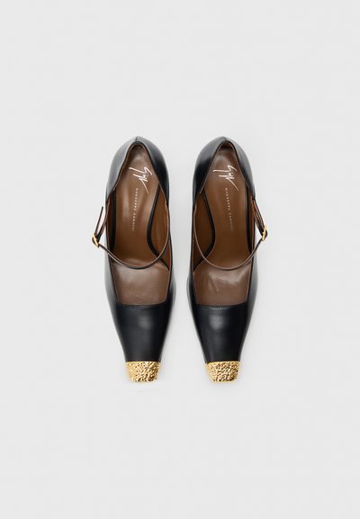 Pantofi cu toc înalt din piele neagră, cu vârf ascuțit, având o căpăcelă texturată aurie și o bretea subțire la gleznă. Branț din piele maro.