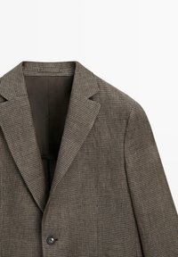 Blazer marrone e grigio con motivo pied de poule, con risvolti a intaglio, chiusura con un bottone e fodera interna scura, mostrato dall'angolo frontale superiore.