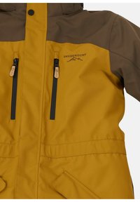 Geel en bruin waterdichte jas met twee ritszakken, een logo en een contrasterend paneelontwerp. Glad materiaal met een matte afwerking.