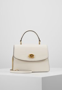 Krämfärgad läderhandväska med en strukturerad design, guldfärgad hardware, ett kort handtag på toppen och ett avtagbart axelband. Har en magnetstängning.