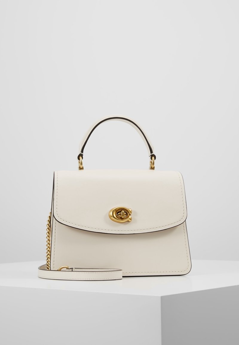 Krämfärgad läderhandväska med en strukturerad design, guldfärgad hardware, ett kort handtag på toppen och ett avtagbart axelband. Har en magnetstängning.