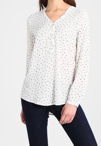 Camicia bianca a maniche lunghe con scollo a V e abbottonatura, caratterizzata da una stampa geometrica piccola ripetuta in rosso, blu e verde.