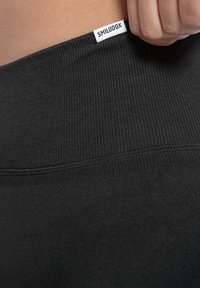 Zwarte geribbelde tailleband van leggings met een wit "SMILODOX" label. De stof lijkt glad en rekbaar, wat een nauwsluitende pasvorm benadrukt.
