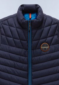 Marinblå pufferväst med hög krage, försedd med diamant-quilting, en blå dragkedja och en rund logotyp på bröstet.