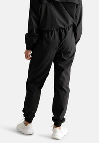 Pantaloni jogger neri realizzati in tessuto leggero, con vita elastica regolabile e caviglie risvoltate, abbinati a sneakers bianche.