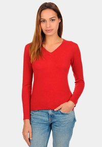 Pull rouge à manches longues en V, fabriqué en tissu doux, avec une coupe ajustée et une texture lisse, assorti à un jean bleu clair.