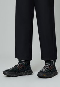 Scarpe da escursionismo nere con tomaia in suede textured, cuciture colorate e lacci riflettenti. Dotate di una suola in gomma maculata per una migliore aderenza.