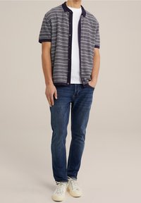Chemise à manches courtes à boutons avec un motif à rayures horizontales en marine, gris et blanc, associés à un jean bleu et des baskets blanches.